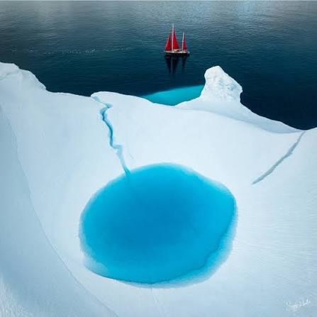 Aerial view of a sailboat navigating through icebergs in Greenland